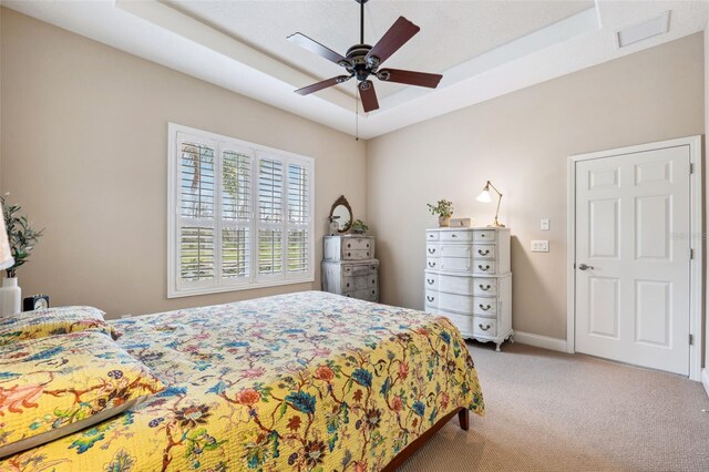 carpeted bedroom with ceiling fan and a raised ceiling