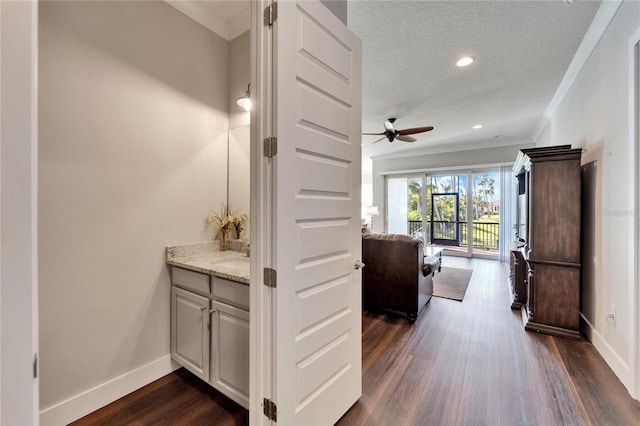 hallway with a textured ceiling, ornamental molding, and dark wood-type flooring