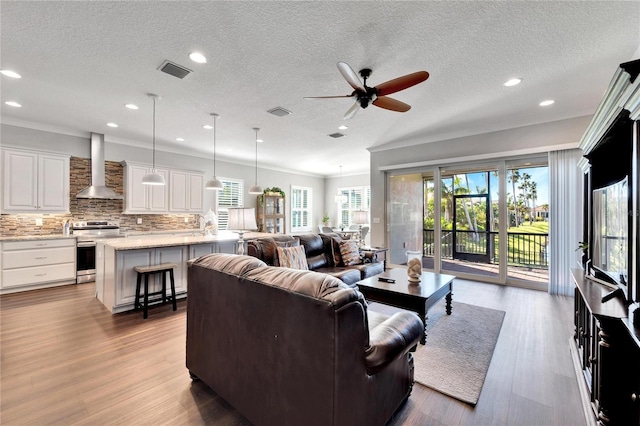 living room with ornamental molding, ceiling fan, light hardwood / wood-style flooring, and a textured ceiling