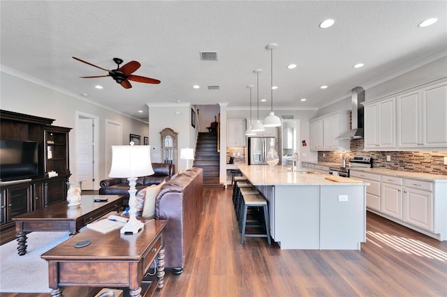 kitchen featuring decorative light fixtures, wall chimney range hood, a large island, white cabinets, and appliances with stainless steel finishes