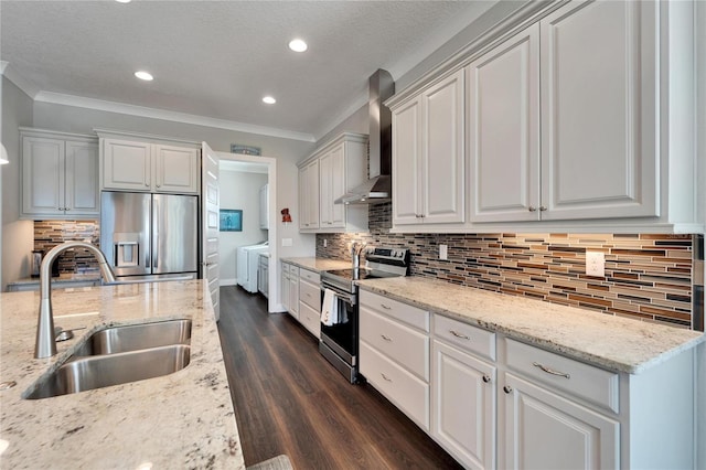 kitchen featuring stainless steel appliances, sink, white cabinets, washing machine and clothes dryer, and wall chimney exhaust hood