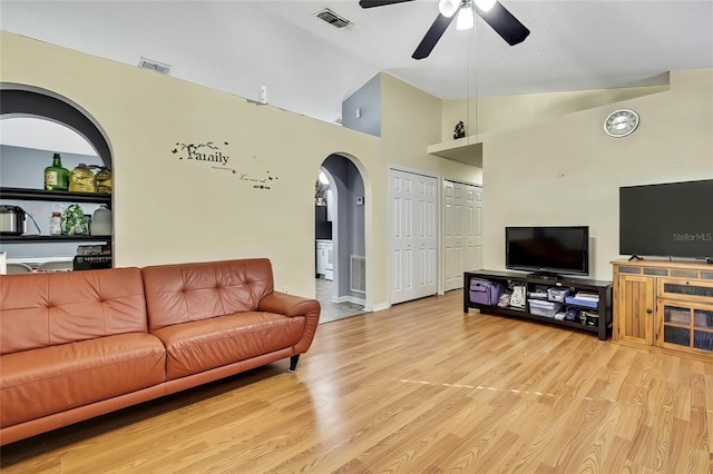 living room with ceiling fan, light hardwood / wood-style flooring, vaulted ceiling, and a textured ceiling