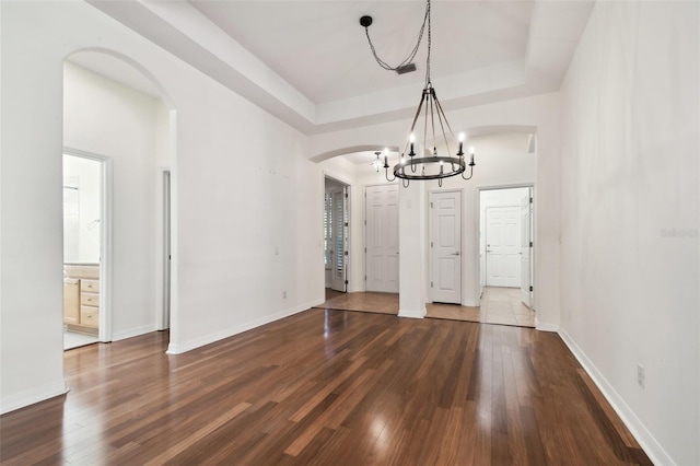 unfurnished dining area with a tray ceiling, an inviting chandelier, and dark hardwood / wood-style floors