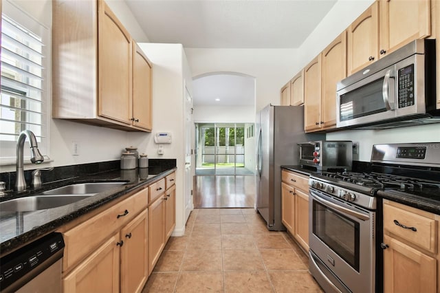 kitchen with dark stone counters, stainless steel appliances, sink, light brown cabinets, and light tile patterned floors