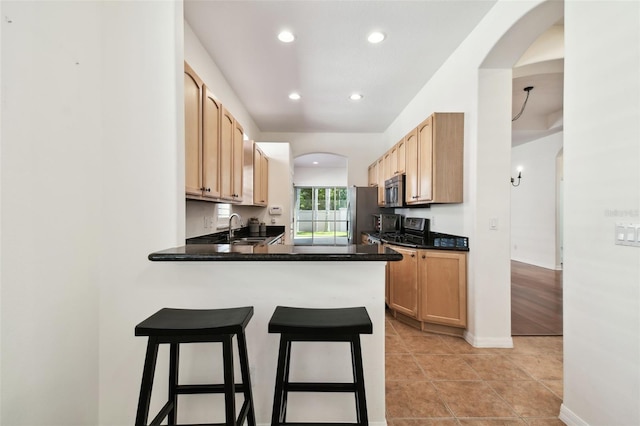 kitchen with kitchen peninsula, appliances with stainless steel finishes, a kitchen breakfast bar, sink, and light tile patterned flooring