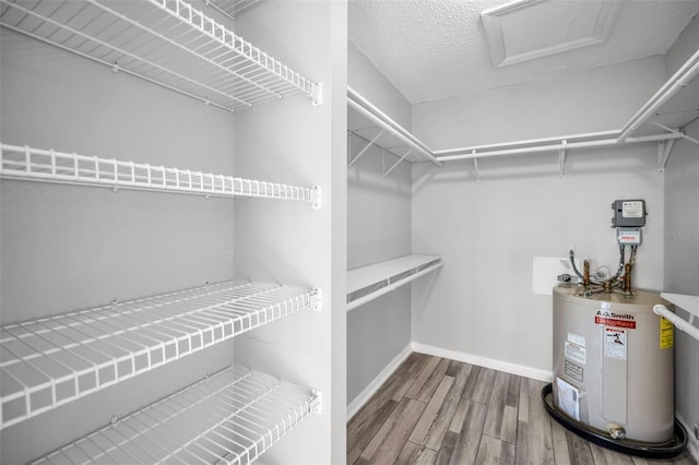 spacious closet with attic access, water heater, and wood finished floors