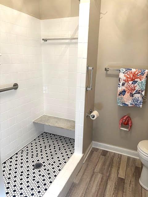 full bath with baseboards, a shower stall, toilet, and wood finished floors