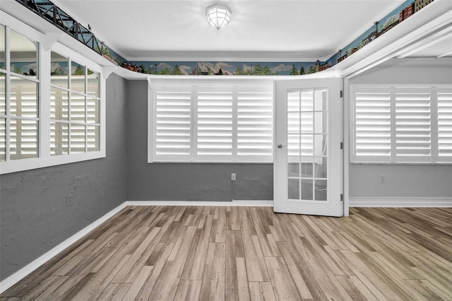 empty room featuring a textured wall, wood finished floors, and baseboards