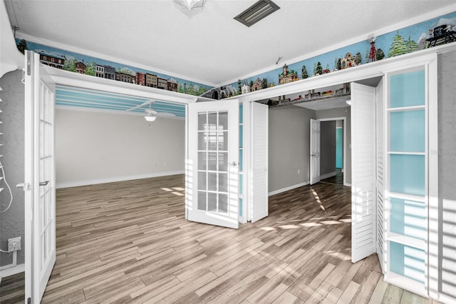 unfurnished room with a textured ceiling, visible vents, wood finished floors, and french doors