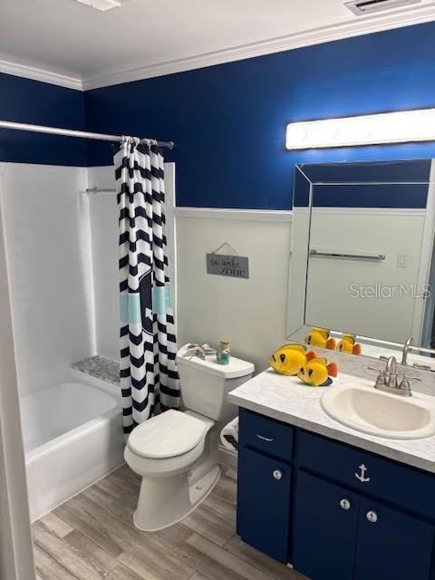 bathroom with toilet, wood finished floors, vanity, shower / tub combo with curtain, and crown molding