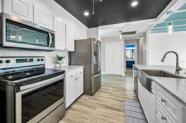 kitchen featuring light stone counters, light wood finished floors, stainless steel appliances, backsplash, and white cabinetry