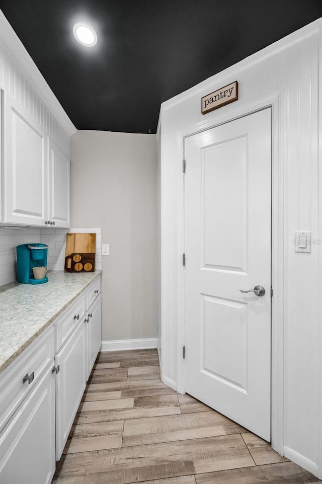 kitchen with light wood-style flooring, white cabinetry, baseboards, light countertops, and backsplash