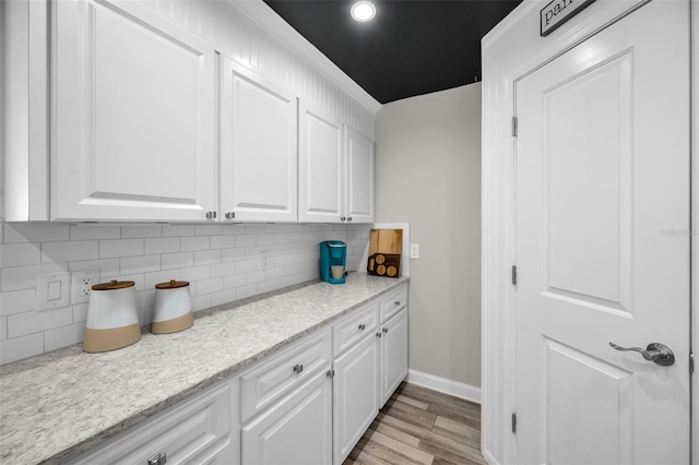 kitchen featuring light wood-type flooring, backsplash, white cabinetry, and baseboards