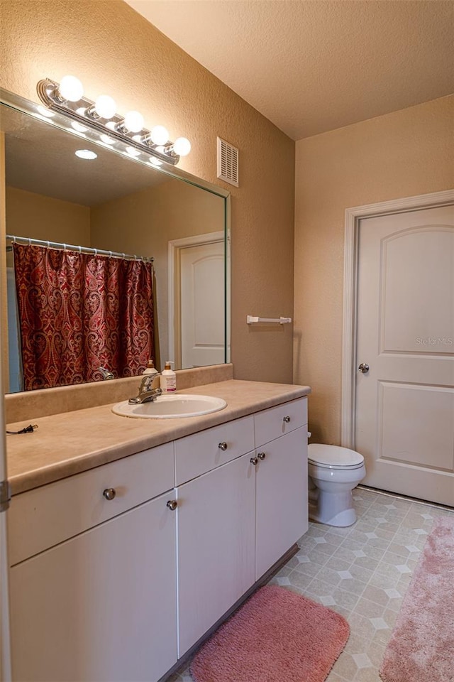 bathroom with a textured ceiling, vanity, and toilet