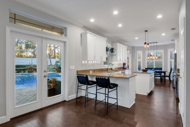 kitchen with sink, kitchen peninsula, hanging light fixtures, a kitchen bar, and white cabinetry