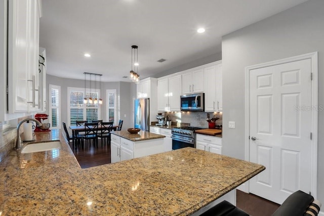 kitchen featuring sink, stainless steel appliances, dark stone countertops, decorative light fixtures, and a kitchen island