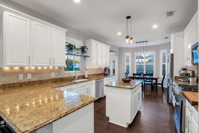 kitchen featuring white cabinets, sink, decorative light fixtures, a kitchen island, and stainless steel appliances