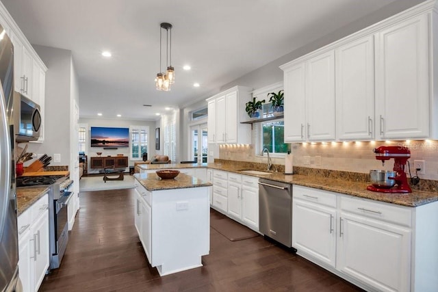 kitchen with kitchen peninsula, appliances with stainless steel finishes, sink, decorative light fixtures, and a kitchen island