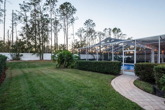 yard at dusk with a lanai and a fenced in pool