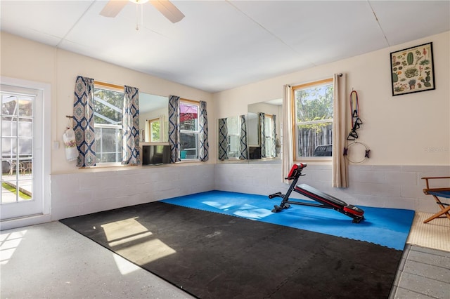 exercise area featuring ceiling fan and concrete block wall