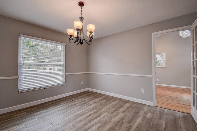 empty room with hardwood / wood-style flooring and an inviting chandelier