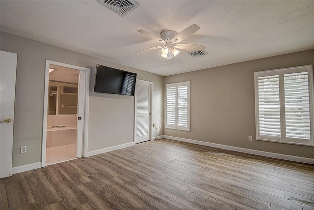 unfurnished bedroom featuring ceiling fan, ensuite bathroom, light hardwood / wood-style floors, and a textured ceiling