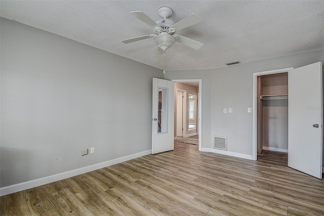 unfurnished bedroom featuring a textured ceiling, a closet, light hardwood / wood-style flooring, and ceiling fan