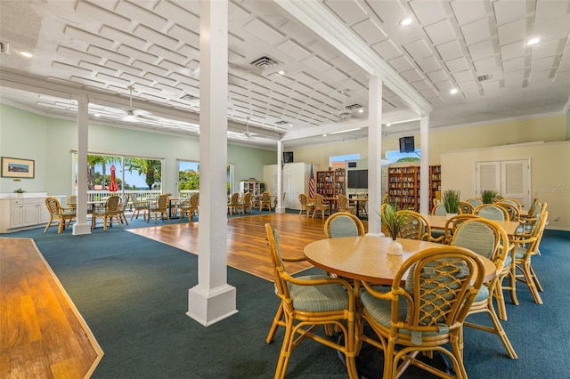 carpeted dining space with crown molding and decorative columns