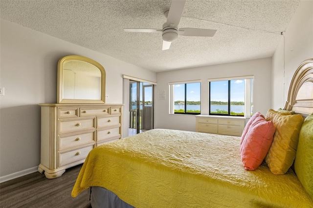 bedroom featuring dark hardwood / wood-style floors, access to outside, ceiling fan, a water view, and a textured ceiling