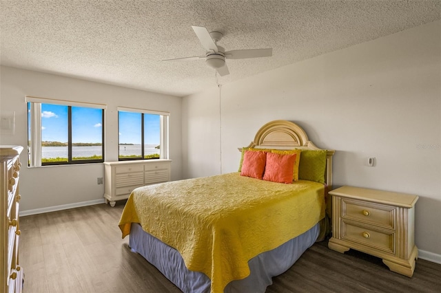 bedroom featuring ceiling fan, a water view, dark wood-type flooring, and a textured ceiling