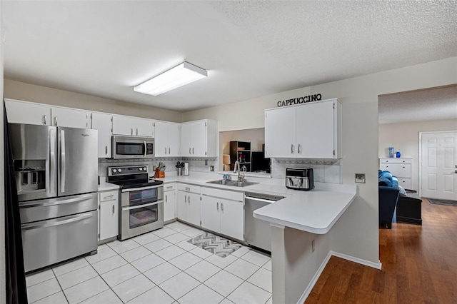 kitchen with appliances with stainless steel finishes, kitchen peninsula, sink, and white cabinets