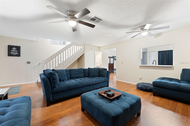 living room featuring hardwood / wood-style flooring, ceiling fan, and a textured ceiling