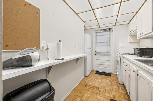 kitchen with white appliances, light parquet floors, sink, decorative backsplash, and white cabinetry