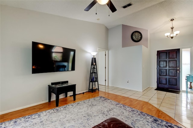 living room with ceiling fan with notable chandelier, light hardwood / wood-style floors, and vaulted ceiling