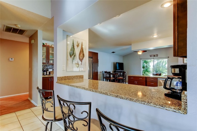 kitchen featuring kitchen peninsula, backsplash, light stone counters, stainless steel appliances, and light tile patterned floors