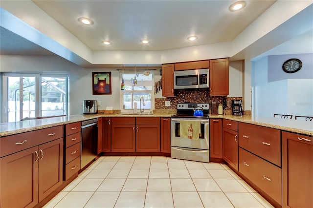 kitchen with kitchen peninsula, light stone countertops, tasteful backsplash, stainless steel appliances, and sink