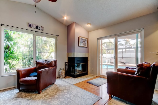 living room featuring a tile fireplace, vaulted ceiling, ceiling fan, light wood-type flooring, and a textured ceiling