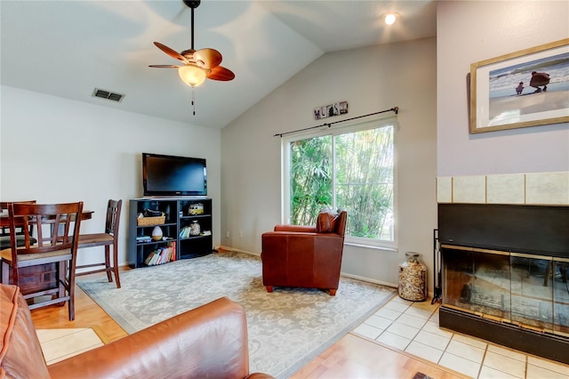 tiled living room featuring ceiling fan, lofted ceiling, and a tiled fireplace