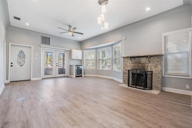 unfurnished living room with french doors, wine cooler, hardwood / wood-style flooring, ceiling fan, and a fireplace