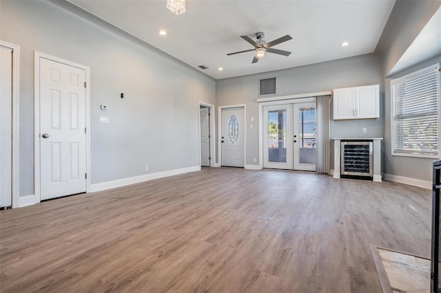 unfurnished living room featuring french doors, light wood-type flooring, beverage cooler, and ceiling fan