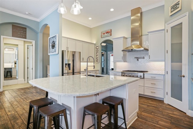 kitchen with stainless steel appliances, decorative backsplash, sink, a kitchen island with sink, and range hood