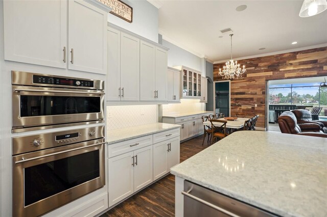 kitchen featuring white cabinetry, stainless steel appliances, wood walls, light stone counters, and crown molding