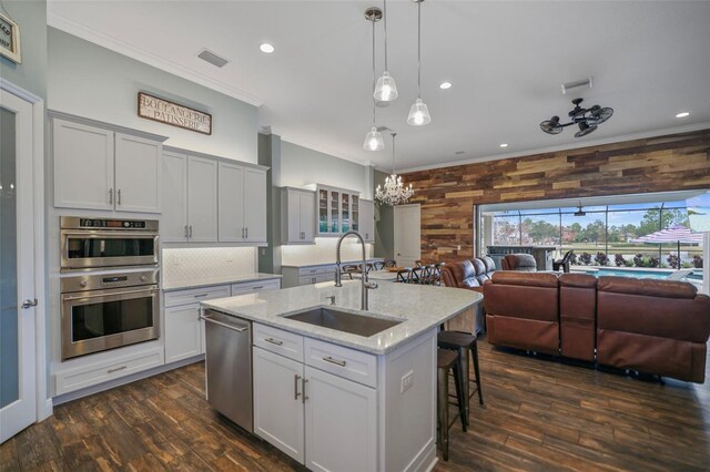 kitchen with wood walls, appliances with stainless steel finishes, a kitchen island with sink, light stone counters, and sink