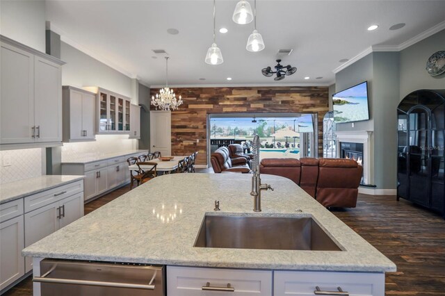 kitchen featuring an island with sink, hanging light fixtures, light stone countertops, crown molding, and stainless steel dishwasher