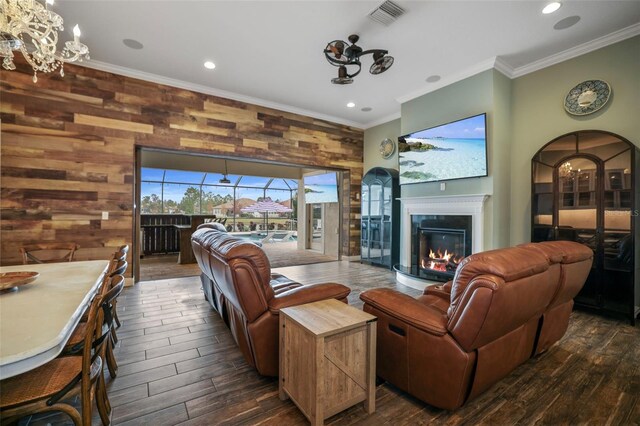 living room with crown molding, ceiling fan with notable chandelier, and wood walls