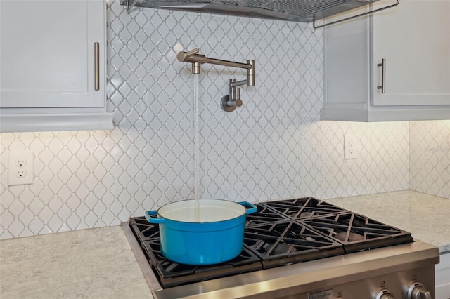 kitchen featuring light stone countertops, extractor fan, white cabinetry, tasteful backsplash, and stainless steel stove