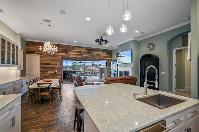 kitchen with decorative light fixtures, sink, a kitchen island with sink, light stone countertops, and ornamental molding