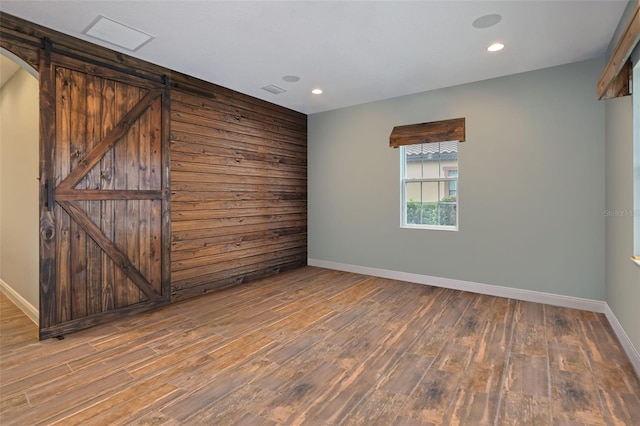 empty room featuring hardwood / wood-style flooring, wood walls, and a barn door