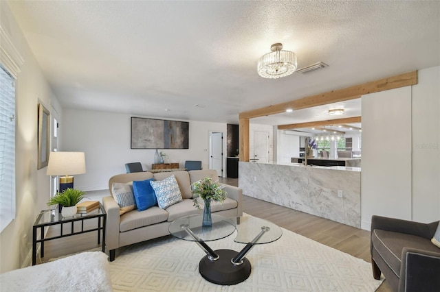 living room featuring beamed ceiling, an inviting chandelier, a textured ceiling, and light hardwood / wood-style flooring