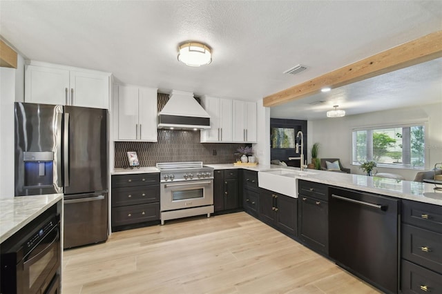 kitchen with custom exhaust hood, sink, stainless steel appliances, and white cabinetry